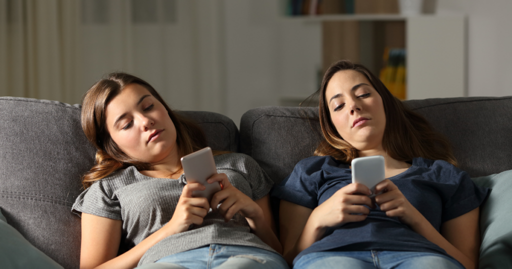 Two friends bored on a couch looking at their phones