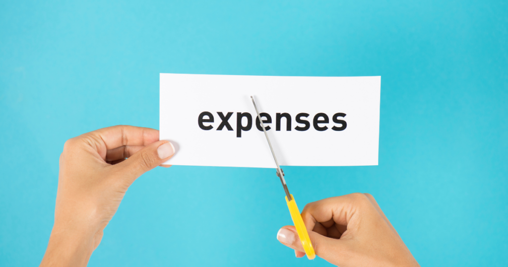 Using scissors to cut paper with the word "expenses" written on it